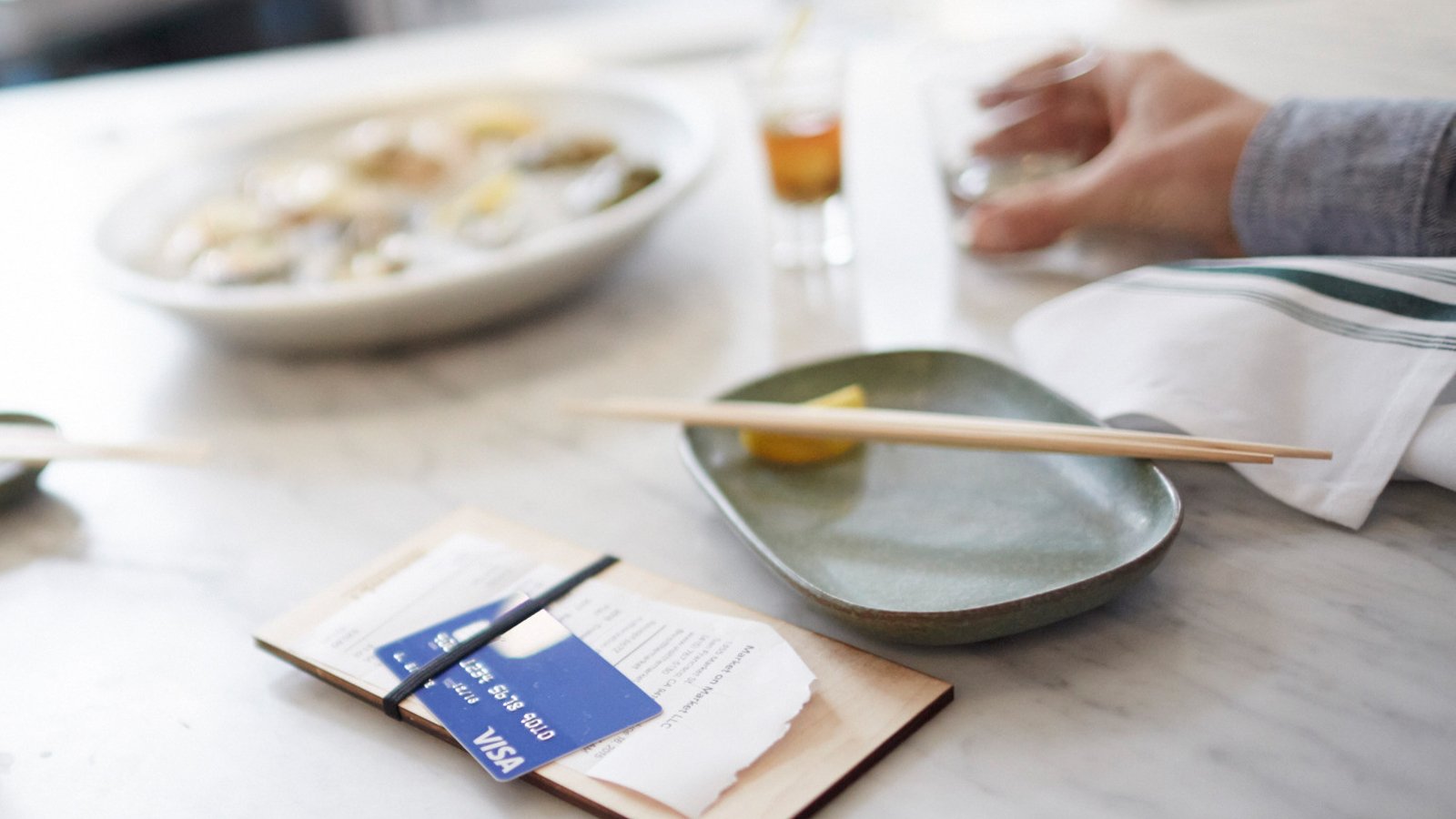 A restaurant table with plates of food and drinks showing a Visa card on top of a check.